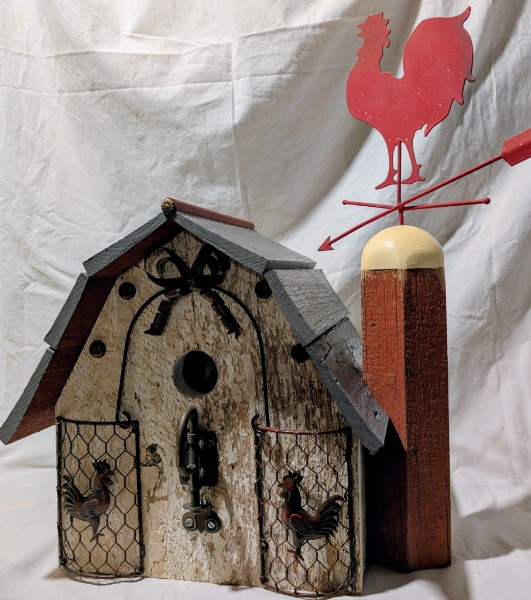 A weathered white birdhouse with wire panels beside a red rooster weather vane.