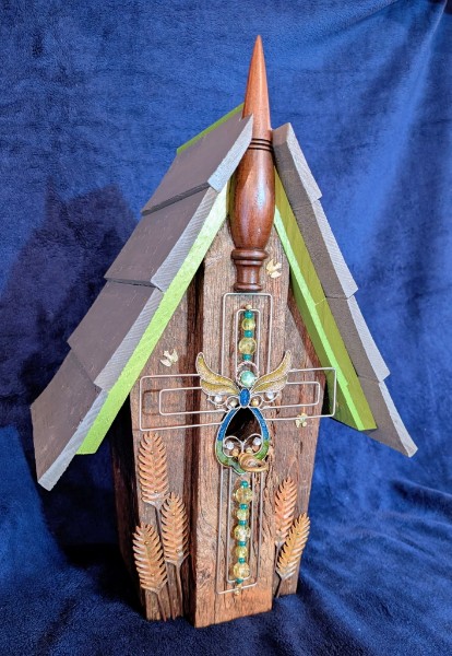 A tall wooden birdhouse with green roof trim, a decorative spindle and a metal dragonfly.